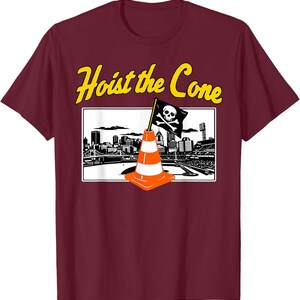 May include: Maroon t-shirt with a graphic featuring an orange and white traffic cone with a skull and crossbones flag, set against a black and white cityscape. The text "Hoist the Cone" is in yellow.