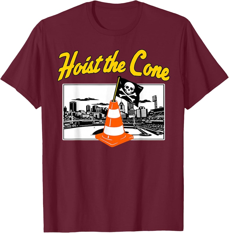 May include: Maroon t-shirt with a graphic featuring an orange and white traffic cone with a skull and crossbones flag, set against a black and white cityscape. The text "Hoist the Cone" is in yellow.