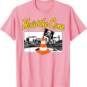 May include: Pink t-shirt with a graphic featuring a traffic cone with a skull and crossbones flag, set against a cityscape. The text "Hoist the Cone" is in yellow above the graphic. A fun, novelty tee.