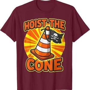 Pu&ograve; includere: T-shirt bordeaux con grafica di un cono stradale con bandiera pirata e le scritte "HOIST THE CONE" e "CONE" in arancione e giallo. Il cono ha strisce bianche e arancioni.