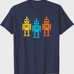 May include: Navy blue t-shirt featuring three colorful robot figures. Each robot is a different color: yellow, blue, and orange. The yellow robot has the number "01", the blue robot has "10", and the orange robot has "11".