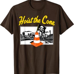 May include: Brown t-shirt with a graphic featuring a traffic cone with a skull and crossbones flag in front of a city skyline. The text "Hoist the Cone" is in yellow.