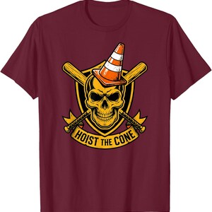 May include: Maroon t-shirt featuring a graphic of a skull wearing an orange and white traffic cone. The skull is set against a yellow shield with crossed baseball bats and the text "HOIST THE CONE".