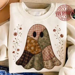 Può includere: Una felpa girocollo color crema con una grafica centrale a forma di fantasma composta da vari motivi di tessuto patchwork in tonalità terra tenui della terra, inclusi quadri e stampe floreali, affiancata da due delicate illustrazioni di tralci fioriti.