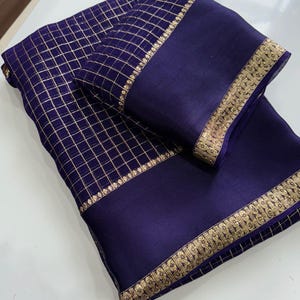 May include: A deep purple fabric piece featuring a gold grid pattern across the main section and a solid purple border adorned with an intricate gold metallic embroidered trim along the edges, folded neatly to display the contrasting textures.