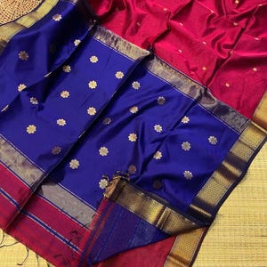 May include: A vibrant saree featuring a deep magenta main body and a contrasting royal blue pallu. Both sections are adorned with small, repeating gold floral motifs. The edges are finished with wide, intricate gold metallic borders.