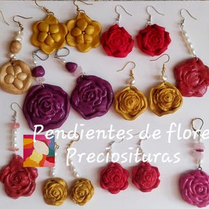 Puede incluir: Una colección de pendientes hechos a mano con diversos diseños florales. Los pendientes presentan formas de rosas y flores doradas, rojas y moradas, algunos con detalles de perlas y piedras preciosas. La imagen incluye el texto "Pendientes de flores Preciosituras".