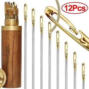 May include: A collection of sewing needles with gold-toned eyes and silver shafts. The needles are displayed with a wooden storage container and a large gold-toned needle with a woven thread. The image includes the text "12Pcs".