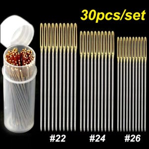 May include: A set of 30 sewing needles in varying sizes, displayed on a black background. The needles are silver with gold-colored eyes. The set includes needles labeled #22, #24, and #26, and are packaged in a clear plastic container.