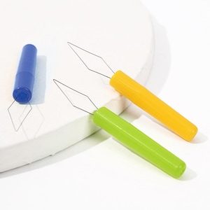 May include: Three needle threaders with cylindrical plastic handles in blue, yellow, and lime green. Each tool features a thin, diamond-shaped wire loop extending from the end of the handle, designed for guiding thread through the eye of a needle.