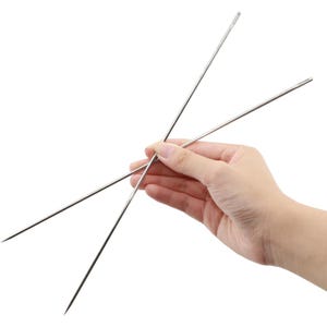 May include: Two long, slender, silver-colored metal needles with pointed tips and eyes at the opposite ends. The needles are positioned in a crossed formation, featuring a smooth, polished finish and a straight, rigid structure for crafting.