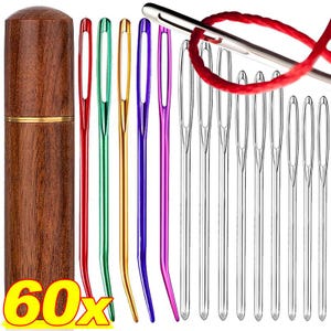 May include: A set of 60 sewing needles with large eyes, including red, green, gold, purple, and silver metal needles, accompanied by a cylindrical wooden storage case. One silver needle is shown threaded with a red yarn strand.
