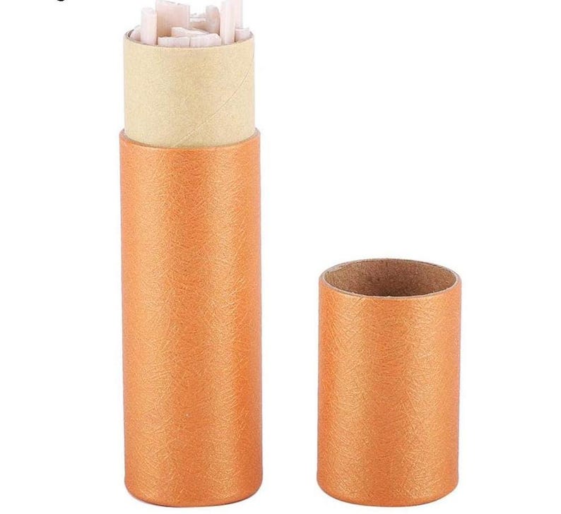 May include: An open, orange cylindrical container with a tan interior, next to a matching orange cylinder. The open container holds several small, white, rectangular objects. The containers have a textured surface.