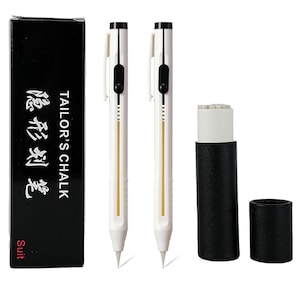 May include: Two white mechanical tailor's chalk pens with black clips and buttons, accompanied by a black storage box labeled "TAILOR'S CHALK" with Chinese characters, and a black cylindrical container with a white chalk refill insert.