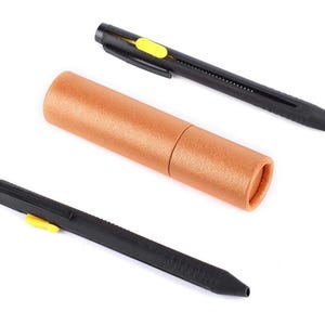 May include: A set of three items: two black lens pens with yellow accents and a cylindrical brown storage case. The pens have a retractable brush tip and a cleaning tip. The case is made of textured brown paper.