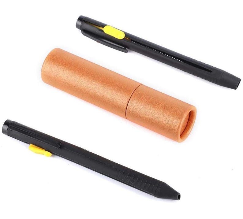 May include: A set of three items: two black lens pens with yellow accents and a cylindrical brown storage case. The pens have a retractable brush tip and a cleaning tip. The case is made of textured brown paper.