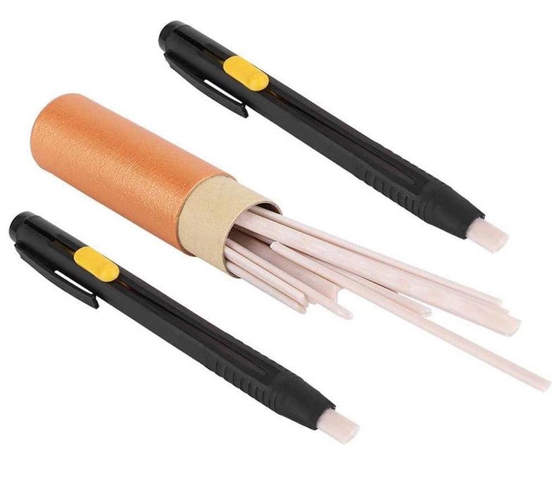 May include: An art supply set featuring a cylindrical container with a brown exterior and a beige interior, filled with numerous light-colored eraser sticks. Two black erasers with yellow buttons are positioned on either side.