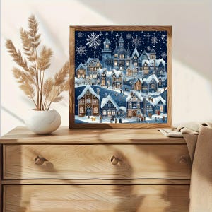 May include: A square framed wall art print depicting a winter village scene at night. The illustration features dark blue tones, snow-covered rooftops, glowing windows, and white snowflakes against a deep blue sky, all encased in a wooden frame.