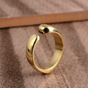 May include: A gold ring with a smooth, polished finish. The ring has a unique open design with rounded ends that curve towards each other. The ring is made of a shiny, yellow metal.