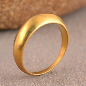 May include: A solid gold ring with a smooth, rounded, and polished surface. The band features a simple, continuous circular design with a consistent width and a warm, reflective metallic finish that catches the light across its curved exterior.