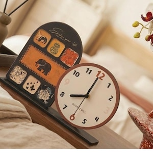 May include: A decorative wooden clock and picture frame set. The clock has a cream-colored face with black numbers and hands, and the frame features an elephant design and the text "Enjoy your life."