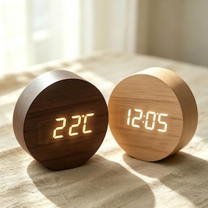 Peut inclure: Deux horloges numériques rondes en bois. L'une est marron foncé, affichant "22C" en ambre. L'autre est en bois clair, indiquant "12:05" en blanc. Design minimaliste et épuré pour ces réveils.