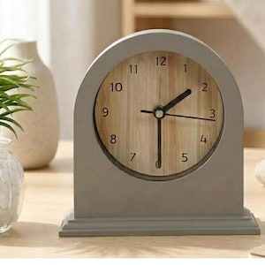Peut inclure: Une horloge de bureau grise en forme d'arche avec un cadran en bois clair. L'horloge a des aiguilles noires et affiche les chiffres de 1 à 12. L'horloge repose sur une base rectangulaire et est un élément de décoration intérieure.