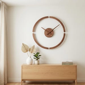 Könnte beinhalten: Eine moderne, minimalistische Wanduhr mit einem kreisförmigen Holzrahmen und einer dunkelbraunen Oberfläche. Die Uhr hat ein zentrales kreisförmiges Zifferblatt und schlanke Zeiger. Die Uhr ist an einer weißen Wand über einem Holzschrank angebracht.
