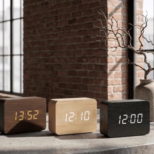 May include: Three wooden digital clocks with rectangular shapes. The clocks display the time in a digital format. The clock on the left is a dark brown color, the middle clock is light brown, and the clock on the right is black.