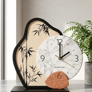 Op de afbeelding: Een decoratieve klok met een marmerlook wijzerplaat, zwarte wijzers en gouden accenten. De klok wordt gecombineerd met een houten paneel met bamboethema en een terracotta-kleurige basis met het nummer 6. De klok staat op een zwarte basis.