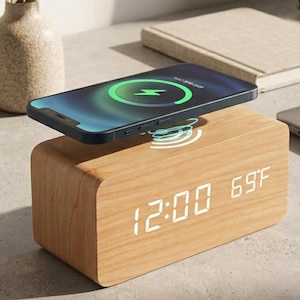 Peut inclure: Réveil numérique en bois avec un socle de chargement sans fil. Un smartphone noir est en charge sur le dessus, affichant un symbole de charge vert. L'horloge affiche l'heure 12h00 et la température 20.5°C.