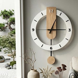 May include: A modern wall clock with a white circular frame and a natural wood-tone center. The clock features black hands and a pendulum. The numbers 12, 3, 6, and 9 are marked. The clock is mounted on a light gray wall.
