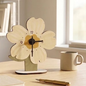 Peut inclure: Une horloge de bureau en bois en forme de fleur avec un cadran crème et des aiguilles noires. L'horloge a un centre jaune et est montée sur une base verte et crème. Une tasse beige et un stylo doré sont sur la surface en bois.