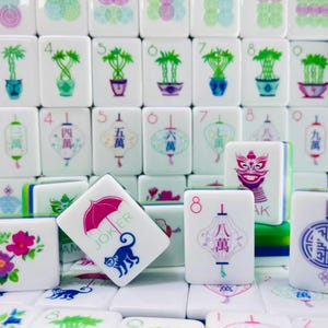 May include: A collection of white Mahjong tiles featuring colorful illustrations of bamboo plants, lanterns, flowers, and a monkey with a pink umbrella. The tiles display various numbers, Chinese characters, and the word JOKER in green text.