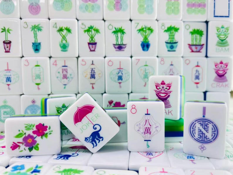 May include: A collection of white Mahjong tiles featuring colorful illustrations of bamboo plants, lanterns, flowers, and a monkey with a pink umbrella. The tiles display various numbers, Chinese characters, and the word JOKER in green text.