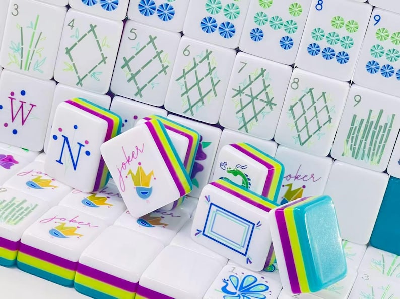 Puede incluir: Una colecci&oacute;n de fichas de Mahjong blancas con dise&ntilde;os coloridos que incluyen tallos de bamb&uacute;, rejillas geom&eacute;tricas, n&uacute;meros y la palabra joker con un icono de corona. Las fichas tienen bordes en capas en tonos brillantes de morado, verde lima y azul.