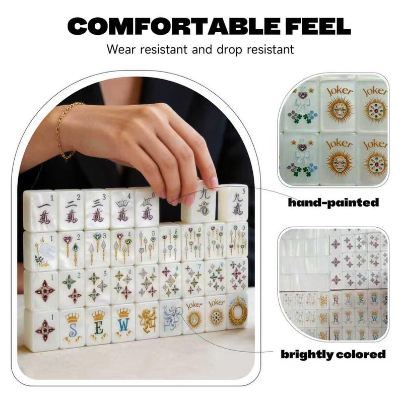 Op de afbeelding: Een set witte rechthoekige mahjongtegels met handgeschilderde, felgekleurde ontwerpen, waaronder cijfers, symbolen, kronen en jokergezichten. De tegels zijn gerangschikt in rijen en kolommen, met de tekst COMFORTABLE FEEL, Wear resistant and drop resistant, hand-painted en brightly colored.