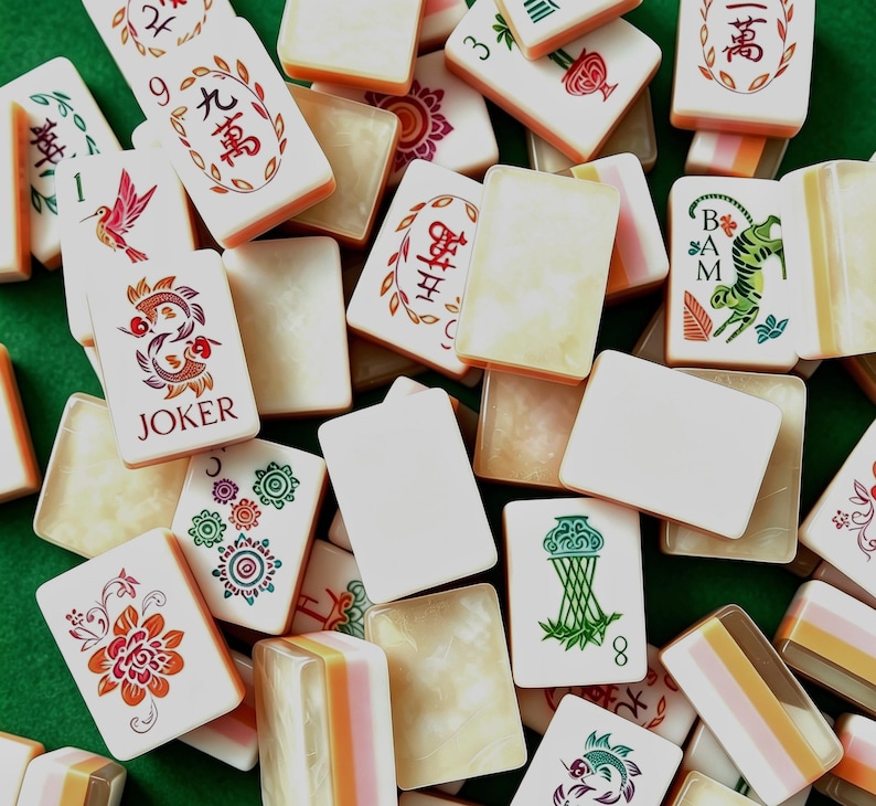 May include: A collection of rectangular mahjong tiles featuring a variety of designs including Chinese characters, a hummingbird, a joker with fish, a tiger, floral patterns, and green bamboo motifs, with some tiles showing blank white or marbled surfaces.