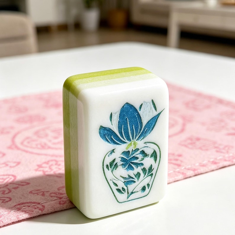 May include: A rectangular mahjong tile with a white front face featuring a blue and green floral design. The sides and back of the tile are a solid light green color. The tile has rounded corners and a smooth, glossy finish on all visible surfaces.