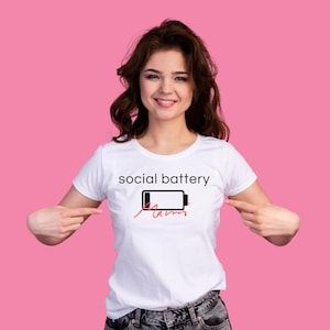Könnte beinhalten: Weißes T-Shirt mit dem Schriftzug "social battery" über einer Grafik eines leeren Akkus. Das Wort "jam" steht in Rot unter dem Akkusymbol. Das T-Shirt wird von einer Person getragen.