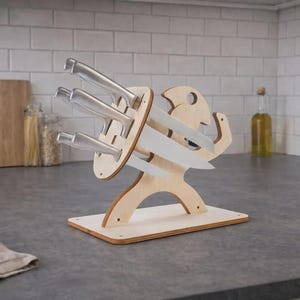 May include: A wooden knife block in a whimsical design, holding several stainless steel knives. The block is light-colored and stands on a rectangular base. The knives are arranged in a fan-like pattern, ready for use in the kitchen.