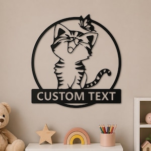 Peut inclure: Décoration murale en métal noir représentant un chat avec un papillon sur la tête, dans un cercle. Le chat a un motif rayé. Une enseigne rectangulaire en dessous indique "CUSTOM TEXT".