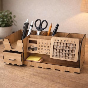 May include: Wooden desk organizer with multiple compartments for pens, scissors, and a calendar. Features a small drawer and a calendar with the days of the week. The organizer is made of light brown wood and sits on a wooden desk.