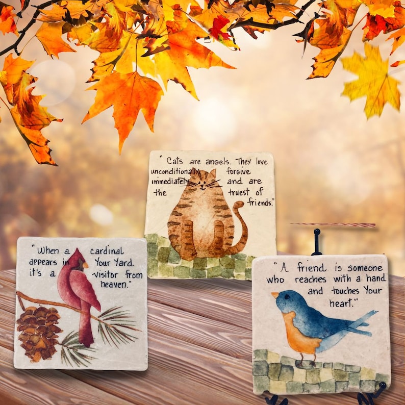 May include: Three decorative stone coasters with inspirational quotes and painted animal illustrations. The first coaster features a cardinal and the quote "When a cardinal appears in your yard it's a visitor from heaven.". The second coaster features a cat and the quote "Cats are angels. They love unconditionally forgive immediately and are truest of friends.". The third coaster features a bluebird and the quote "A friend is someone who reaches with a hand and touches your heart."
