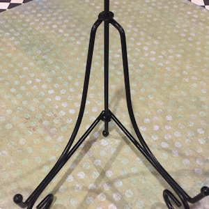 May include: Black metal display stand with a triangular base and a curved top. The stand is designed to hold a plate or other flat object.