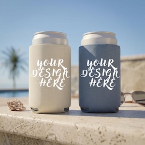 Könnte beinhalten: Zwei Getränkedosenkühler, einer beige und einer blau, jeweils mit einer weißen Dose im Inneren. Die Kühler tragen den Text "YOUR DESIGN HERE" in einer Schreibschrift. Eine Muschel und eine Sonnenbrille sind im Hintergrund.