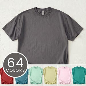 Könnte beinhalten: Ein dunkelgraues T-Shirt mit Rundhalsausschnitt und kurzen Ärmeln. Eine kreisförmige Grafik zeigt "64 FARBEN" mit einer Vielzahl von T-Shirt-Farben darunter, darunter Rot, Türkis, Mintgrün, Gelb, Rosa und Türkis.