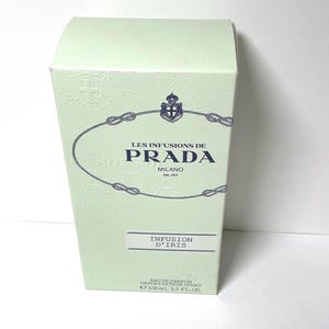 Peut inclure: Une boîte de parfum rectangulaire vert pâle avec le texte Les Infusions de Prada Milano dal 1913, un emblème de corde bleu marine et une étiquette Infusion d'Iris. Le texte en bas indique Eau de Parfum Vaporisateur Spray 100ml 3.3 FL. OZ.