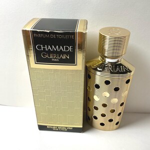 May include: A Guerlain Chamade parfum de toilette refillable natural spray bottle and its matching rectangular box. The gold-toned bottle features a ribbed texture with circular cutouts. The box displays the text Chamade Guerlain Paris 50 ml 1.7 FL OZ.