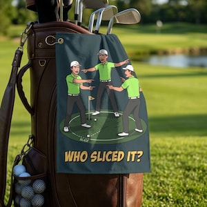May include: A dark gray golf towel hanging from a brown leather golf bag. The towel features a graphic of three golfers in lime green shirts and gray pants pointing at each other on a green, with the text "WHO SLICED IT?" printed in yellow.